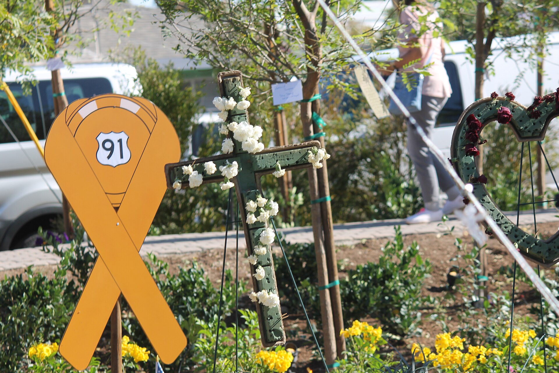 Yellow Route 91 remembrance ribbon beside a flowered memorial cross in the Las Vegas Community Healing Garden